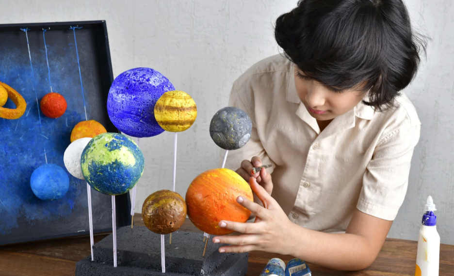 Boy with black hair painting model solar system. 