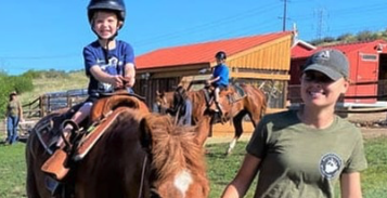 Little girl riding horse being led by instructor. 