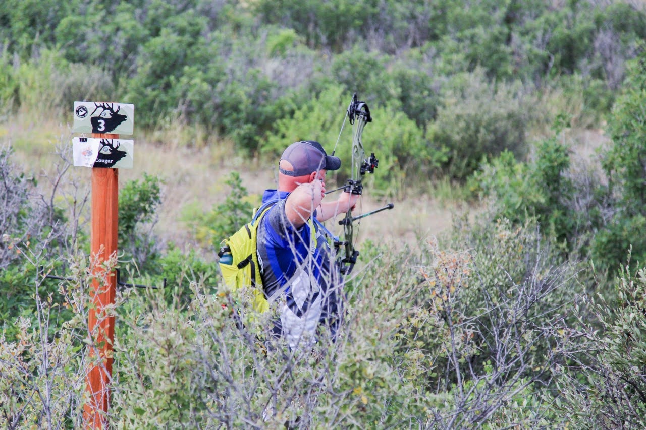 Man in field aiming a bow and arrow